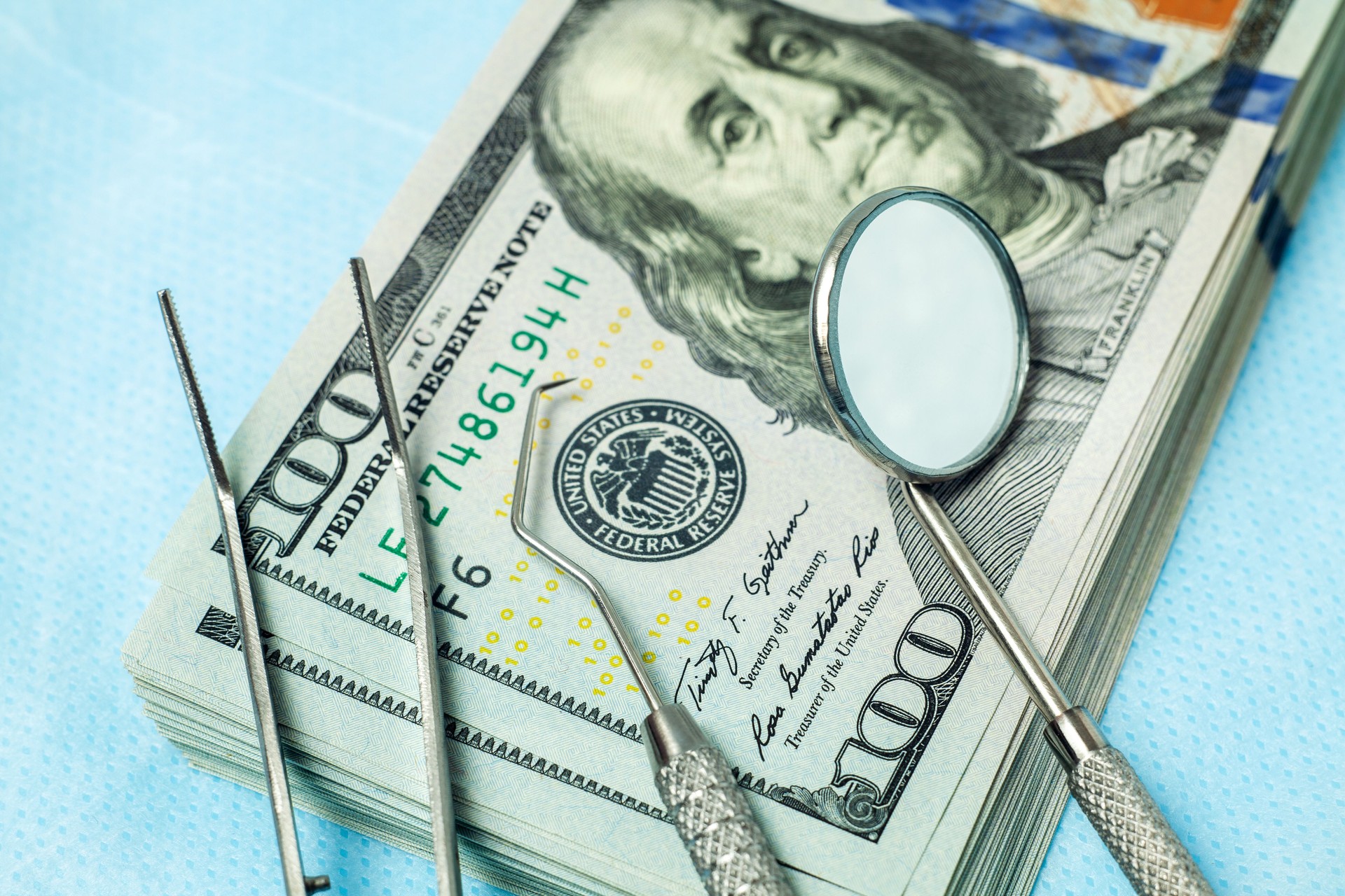 Dental tools mirror, tweezers and a hook on a stack of cash dollar bills. Concept expensive dentistry or dental insurance